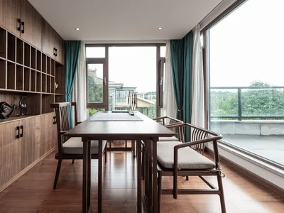 Interior of a modern home office with wooden furniture and large windows overlooking greenery.