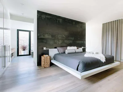 A modern minimalist bedroom featuring wooden flooring, a floating bed, and a dark accent wall.