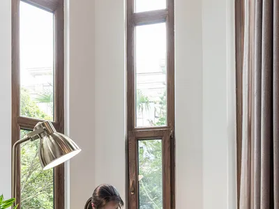 A person wearing glasses is reading a book in a cozy, industrial-style living room with wooden furniture and plants.