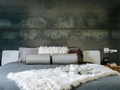 A minimalist bedroom with a faux concrete headboard and a plush white wool blanket, featuring modern and sleek design element