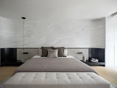 A minimalist bedroom with a marble-patterned wall, a large bed, and a tufted bench.