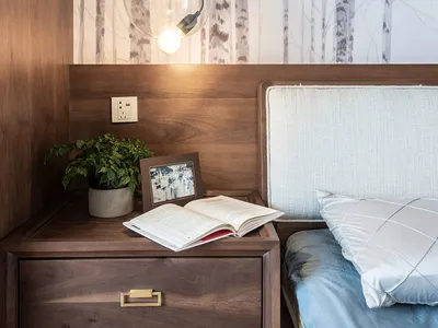 A modern minimalist bedroom featuring a wooden bed frame and nightstand with a potted plant, an open book, and a spherical pe