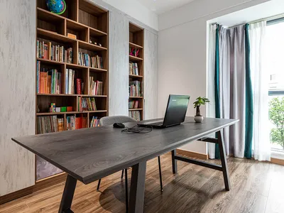 A modern home office featuring a wooden desk and floor-to-ceiling bookshelf.