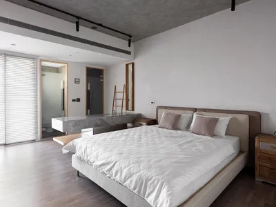 A minimalist bedroom featuring a bed with a concrete headboard and wooden furniture, in a modern industrial style.