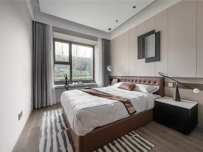 A minimalist bedroom featuring a brown leather bed, wooden floors, and fabric bedding.