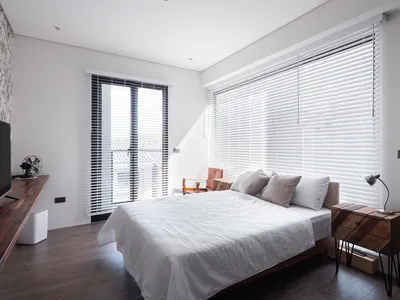 A minimalist bedroom with a large bed, white bedding, and white blinds covering the windows.