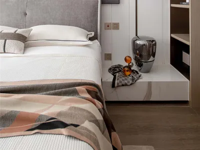 A modern bedroom featuring a bed with a fabric headboard, metallic vase, and wooden shelving unit.