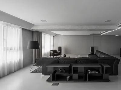 A minimalist living room with black furniture, concrete walls, and a large floor lamp.