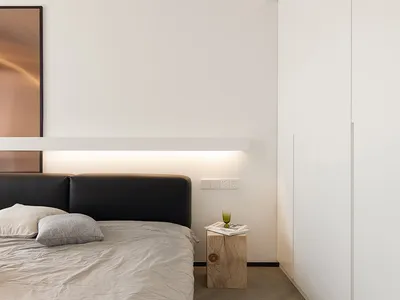 A minimalist bedroom featuring a black bed frame with a wooden headboard, grey bedding, and a wooden side table with a book a
