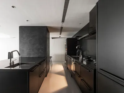 Interior view of a modern minimalist kitchen featuring black cabinets, metallic countertops, and stainless steel appliances.