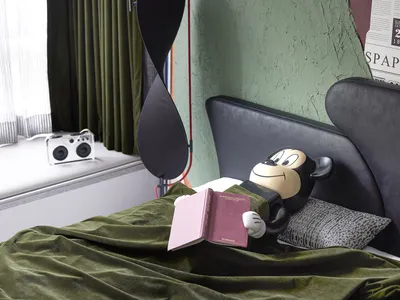 A modern bedroom with a black bed featuring a geometric pillow, green curtains, a green blanket, and a white speaker on the w