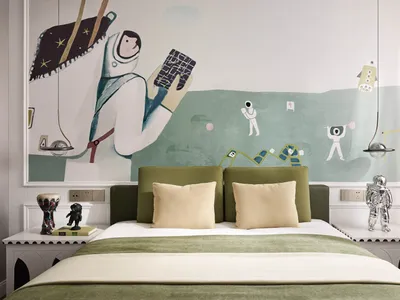 A minimalist bedroom featuring a green upholstered headboard and a playful, astronaut-themed mural on the wall.