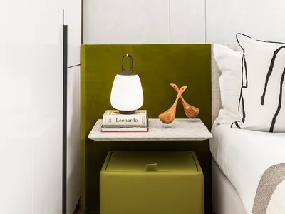 A minimalist bedroom featuring a green nightstand with a lamp, books, and wooden figurines.