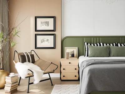 A modern bedroom with a green upholstered headboard, white bedding, and a cozy sitting area with a woven chair and sheepskin