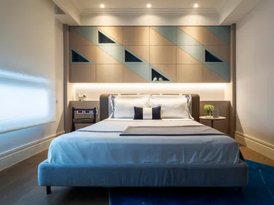 Minimalist bedroom with gray upholstered bed, geometric wall paneling, and blue rug on hardwood floor.
