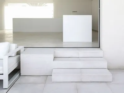 A minimalist living room with concrete flooring and stairs leading up to a modern interior.