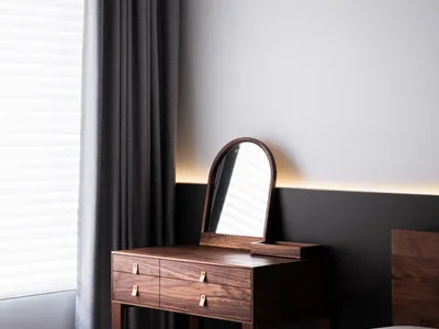 A minimalist bedroom featuring a wooden console table with a built-in mirror and drawers, complemented by natural light strea