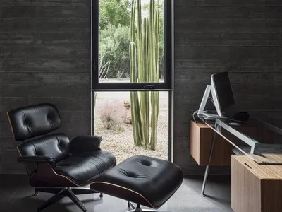 A minimalist home office featuring wooden furniture and a large windowsill, with a cactus plant and outdoor greenery seen thr