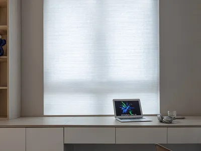 A modern home office setting featuring a wooden desk with a laptop, headphones, and a glass of water.