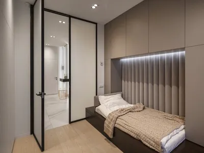 A modern bedroom with neutral colors and minimalist design features a single bed with a padded headboard, wooden floor, and b