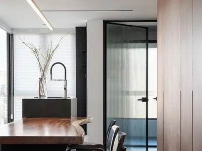 Modern kitchen with wooden counter featuring black and white stools and a sink with a black faucet.