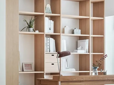 A minimalist home office featuring light wood shelves, a wooden desk, and a grey sofa.