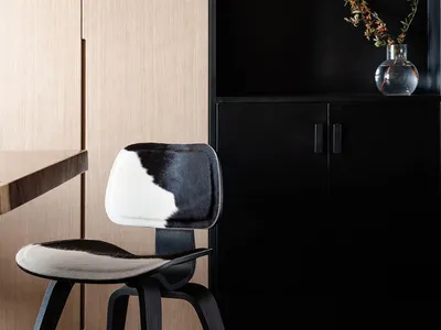 A modern home office features a black cabinet, a cowhide-covered chair, and a round mirror on a dark wall.