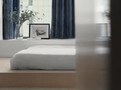 Minimalist bedroom with a wood frame bed, white bedding, and blue curtains.