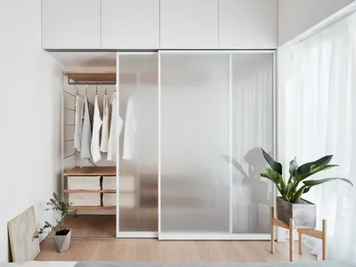 A minimalist bedroom with a glass sliding door, white furniture, and light wood flooring.
