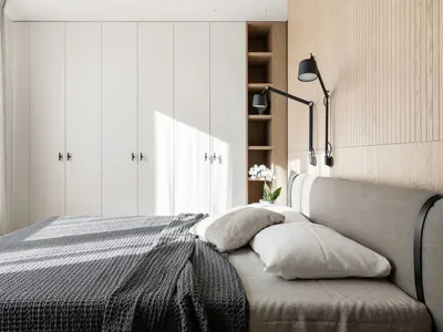 Modern minimalist bedroom featuring a grey upholstered bed against a wall of light wood panels and a large white wardrobe.