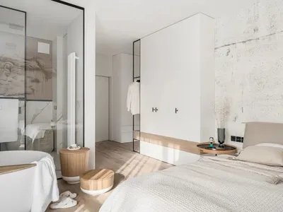 A modern minimalist bedroom with light wood flooring, marble countertops, and white walls.