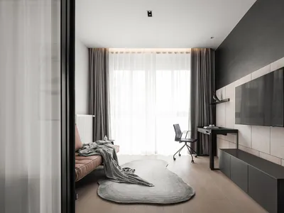 A minimalist living room featuring gray curtains, a leather armchair, a desk with a flat-screen TV, and a wooden floor.