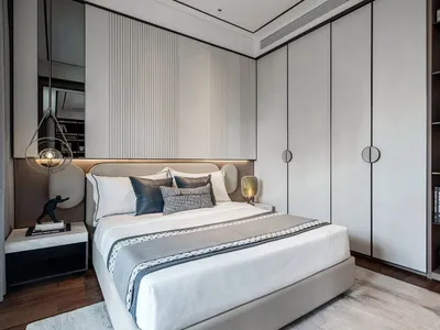 A modern minimalist bedroom featuring a white bed with fabric and metal accents, surrounded by wooden furniture and a large w