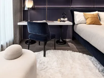 A modern minimalist bedroom with black walls and a white desk, featuring a white fur rug and a circular light fixture.