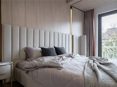 Modern minimalist bedroom with a white upholstered headboard, gray bedding, and pink curtains against a window with a view of