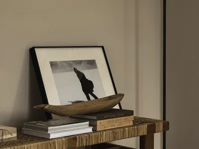 A candlestick with a wooden bowl, books, and a framed black-and-white photograph on a woven bench in an industrial-style livi