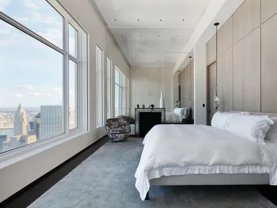 Modern minimalist bedroom with a large window, white bedding, and a floral armchair.