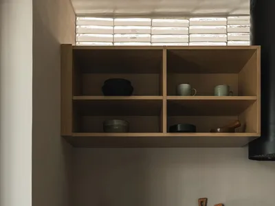 Modern kitchen with open shelving and wooden cabinets, featuring ceramic cups and wooden cutting board.