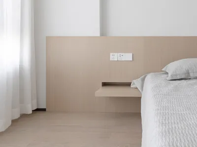 A minimalist bedroom featuring a floating wood shelf next to the bed and a white curtain.