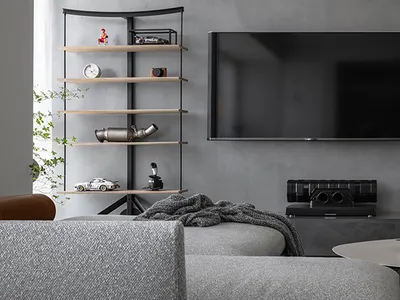 Modern living room featuring industrial decor with concrete walls, black armchair, and a grey sofa with throw blankets.