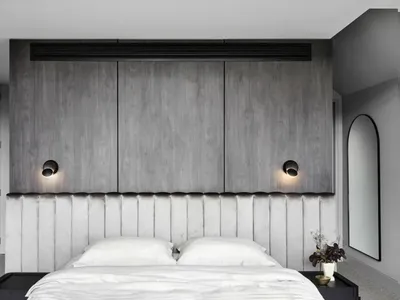 A minimalist bedroom with a wooden headboard and white bedding, featuring grey walls and a mirrored accent wall.