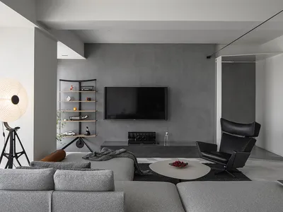 Modern minimalist living room with concrete walls, furniture, and floor, featuring a grey sectional sofa, a round coffee tabl