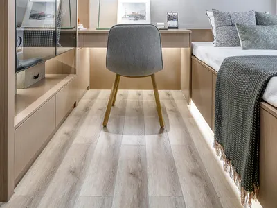 A modern minimalist bedroom with wooden flooring, furniture, and shelves. Features a working area with a desk, chair, and vis