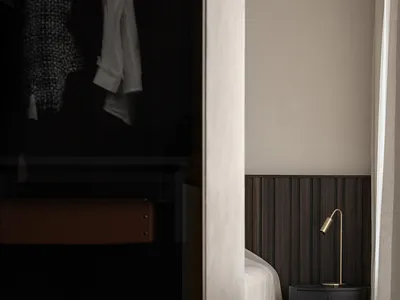 A minimalist bedroom with dark wood furniture, white bedding, and a brass bedside lamp.