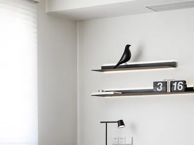 A minimalist home office featuring a wooden desk, black chair, and a black bird sculpture on a floating shelf.