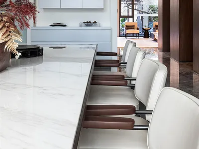 Modern kitchen interior with white marble countertops and chairs.