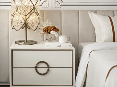 A serene minimalist bedroom featuring a fabric upholstered bed, a side table with a crystal lamp, and a vase of dried flowers