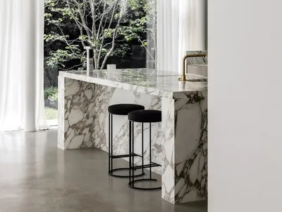 Modern kitchen with marble countertop and black stools, featuring large windows with white curtains.