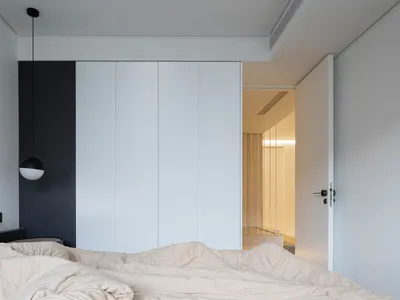 Modern minimalist bedroom with white cabinets and a bed with a neutral-colored blanket.