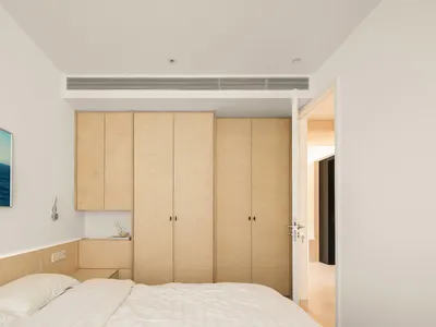 A minimalist bedroom featuring wood cabinets and a bed with white sheets and pillows.